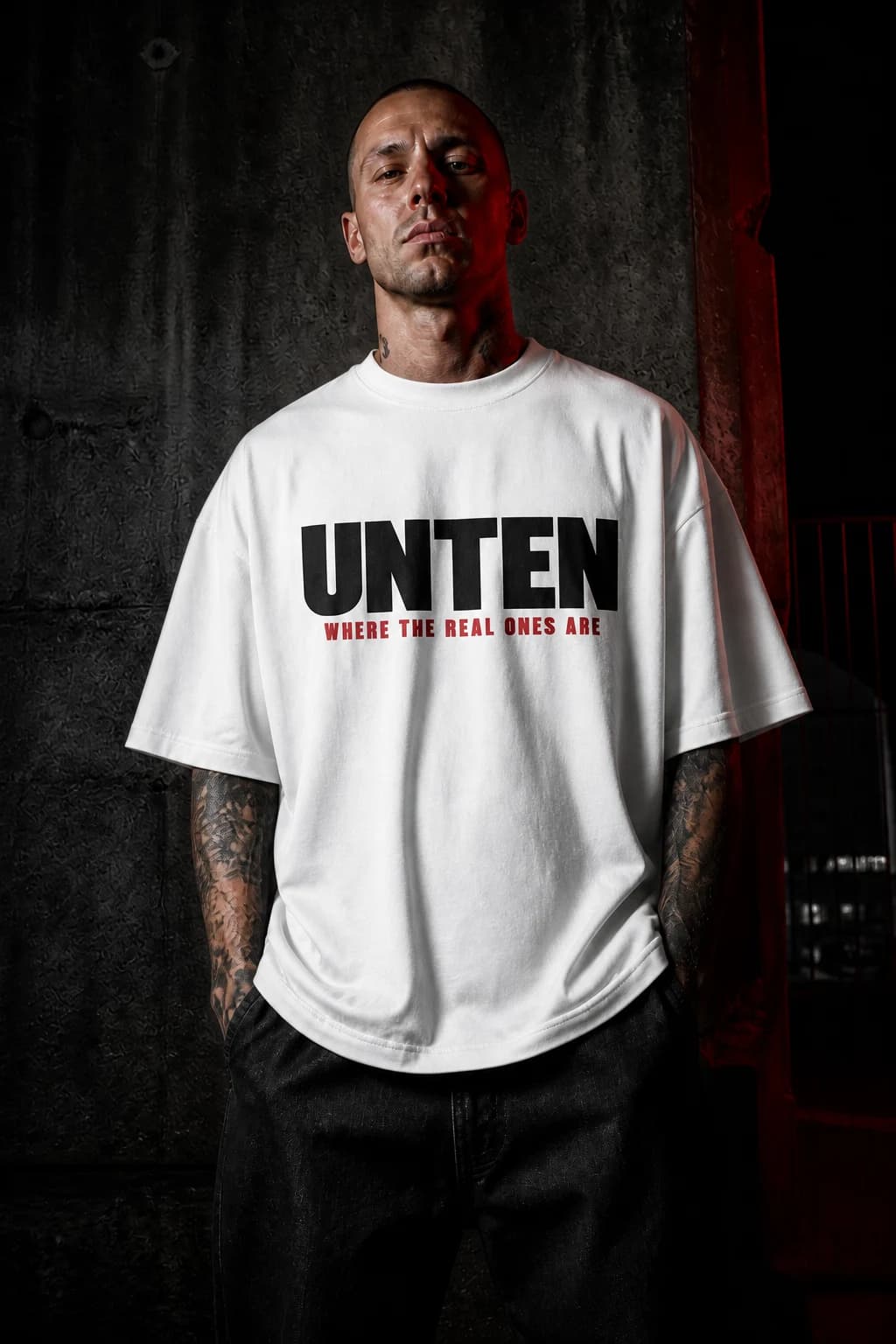 Person im weißen UNTEN Oversize-T-Shirt vor einer Betonwand