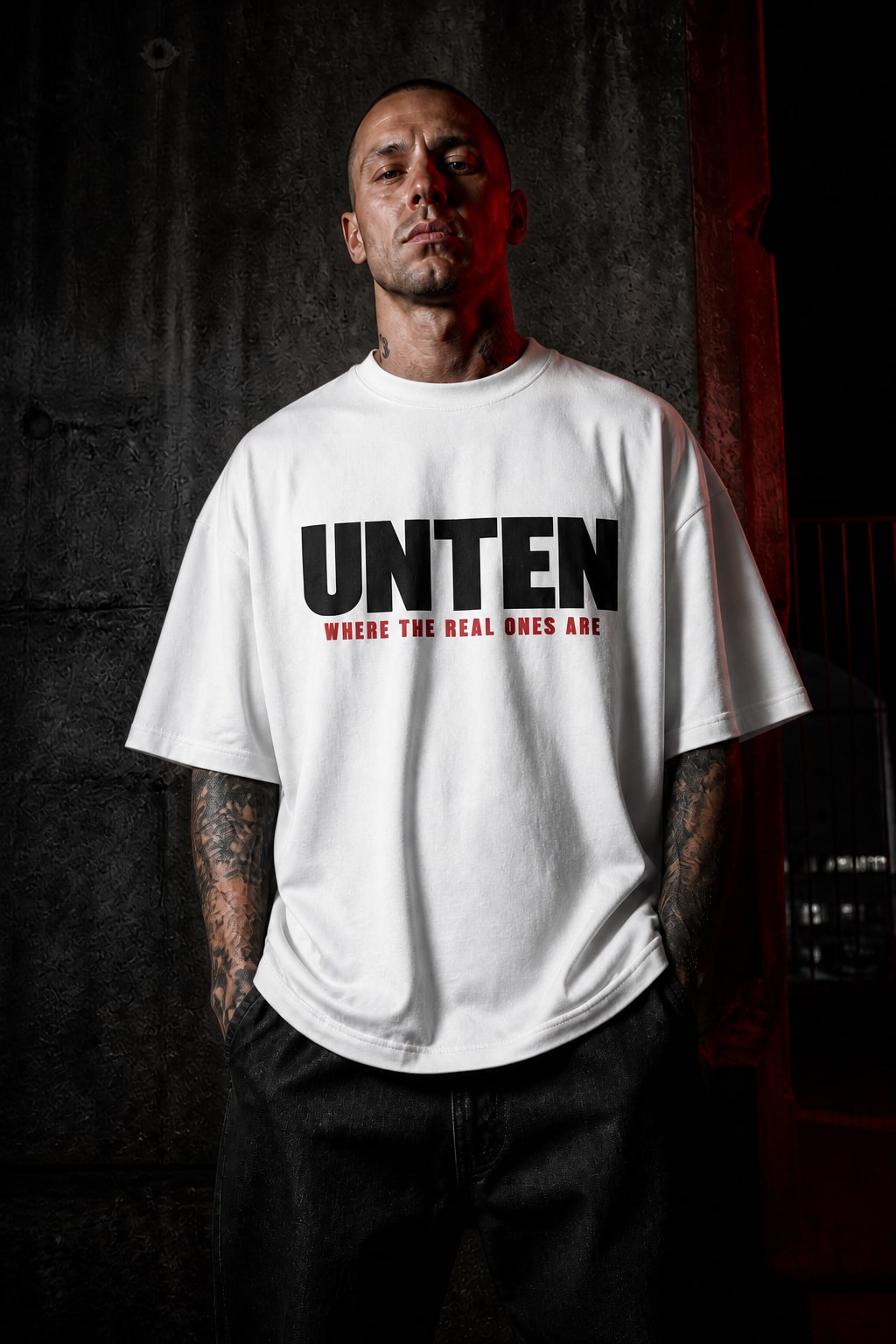 Person im weißen UNTEN Oversize-T-Shirt vor einer Betonwand